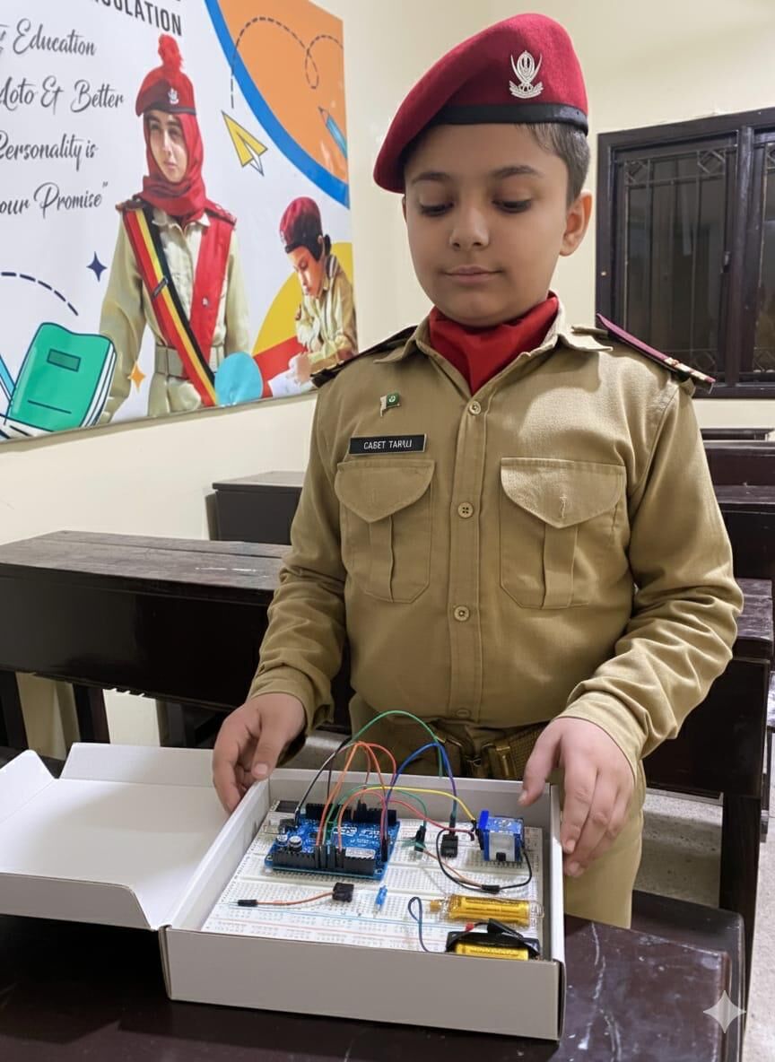 A cadet in uniform and beret holding up a robotics project